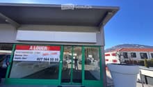 Commercial building with glass doors and windows, green frame, signboard, and a large white planter