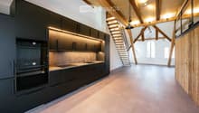 Modern kitchen with black cabinets, stainless steel appliances, and a sleek design, featuring a staircase leading to an open loft area.