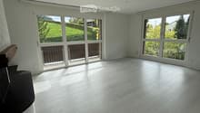 Empty room with light-colored wooden flooring, large windows, and a view of a green landscape.