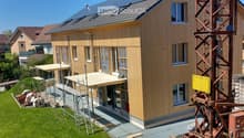 Newly constructed house, wooden exterior, solar panels on the roof, scaffolding around the building, construction crane nearby