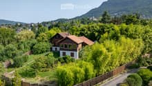 detached house with tiled roof, surrounded by green trees, situated in a scenic area with mountains