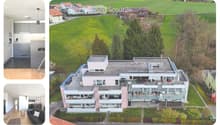Aerial view of a modern apartment building with multiple balconies, surrounded by a green field and trees, with a clear view of the surrounding landscape.