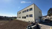 Modern white building, multiple windows, under construction, large empty field in front