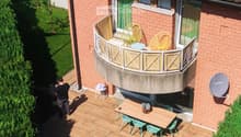 Wooden deck area with a sofa, coffee table, dining table, chairs, and a small balcony with additional seating.
