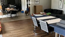 Living room with hardwood flooring, a sofa, coffee table, and a dining area with a table and chairs visible in the background.