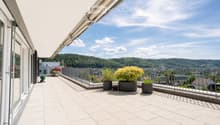Balcony with white tiled floor, metal railing, potted plants, and a scenic view of a green, hilly landscape.