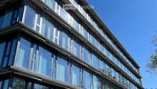 Modern multi-story building with large glass windows and a sleek, contemporary design. The structure features clean lines and a combination of glass and concrete materials.