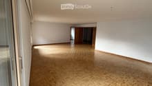 Empty room with wooden herringbone flooring, white walls, and large windows. No furniture or equipment visible.