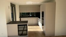 Modern kitchen with light-colored cabinets, black countertops, and wooden flooring. Features include a sink, faucet, oven, and dishwasher.