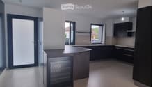 Modern kitchen with dark cabinets, a central island, and a built-in refrigerator. The space features large windows and a sleek, contemporary design.