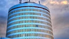 A modern, cylindrical skyscraper with reflective glass windows and a rounded top, featuring communication antennas on the roof.