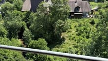 Balcony overlooking a rural landscape with scattered houses, trees, and open fields under a partly cloudy sky.