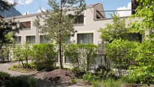 Building. Modern two-story house with white exterior, large windows, and surrounding greenery including trees and shrubs.