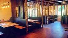 Restaurant interior with wooden tables, benches, and hanging lamps, featuring birch tree trunks as decorative columns.