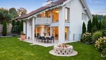 House. Modern two-story house with white exterior, large windows, and a spacious garden featuring a dining set, fire pit, and well-maintained lawn.