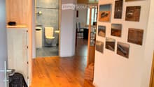 Corridor / Hallway. A well-lit hallway with wooden flooring, white walls, and several framed pictures. A small bathroom is visible to the left, and a dining area is visible to the right.