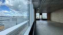 Modern balcony with large glass windows, concrete floor, and a view of the cityscape and surrounding buildings.