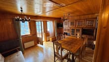 Cozy wooden-paneled room with a dining area, sofa, and cabinetry, featuring large windows and a chandelier.