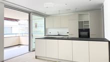 Modern kitchen with white cabinets, black countertop, sink, faucet, and built-in oven. Large sliding glass door provides access to an outdoor area.