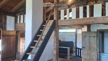 Loft-style room with wooden beams, exposed wooden floor, a wooden staircase leading to an upper level, a sofa, and potted plants on the upper level.