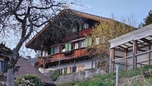 Two-story wooden house with green shutters, wooden balcony, and covered patio area.