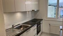 Modern kitchen with white cabinets, stainless steel sink, oven, and a window offering a view of the surrounding area.