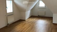 Empty attic room with wooden flooring, white walls, and two windows with slanted ceilings.
