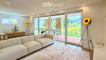 Living Room. Modern living room with large sliding glass doors opening to a patio, a sectional sofa, ottoman, coffee table, floor lamp, side table, and dining area with chairs and a table.