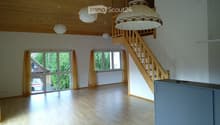 Bright, empty room with wooden flooring, large windows with yellow curtains, wooden staircase leading to an upper level, and several hanging lamps.