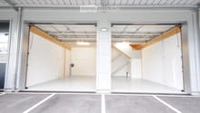 Modern, spacious garage with two large open doors, clean white interior, and a concrete parking area outside.