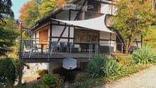 Traditional half-timbered house with a spacious wooden balcony, outdoor furniture, and surrounding garden area.