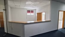 Empty office space with a reception desk, white walls, carpeted floor, and multiple doors leading to other rooms.