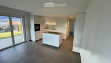 Modern kitchen with white cabinets, a central island, built-in oven, and a sink. The space features large windows and a view of the outdoor area.