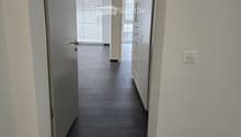 Clean, modern hallway with dark tiled floor, white walls, and a ceiling light. Features a partially open door leading to another room and a staircase with granite steps.