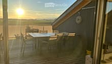 Wooden deck with a table and chairs, overlooking a scenic landscape at sunset.