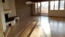 Empty room with wooden floor, exposed wooden ceiling beams, stone accent wall, large windows, and sliding glass doors leading to a balcony.