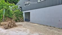 Modern two-story building with grey exterior, raised ground floor, and a paved driveway.
