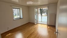 Empty room with wooden flooring, white walls, large window, and sliding glass door leading to a balcony.