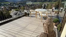 A balcony with a table and chairs, a statue, and a view of the mountains and town