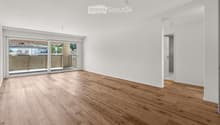 Empty room with light wooden flooring, white walls, and large sliding glass doors leading to a balcony.