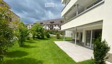 Well-maintained garden with green lawn, trimmed bushes, and a modern house with large windows and a balcony.