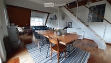 Bright living and dining area with wooden floors, a large dining table with chairs, a sofa, a staircase, and modern decor including a patterned rug and pendant lights.