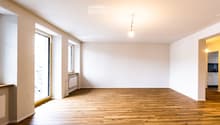 Empty room with wooden flooring, white walls, and large windows allowing natural light. No furniture or equipment is present.