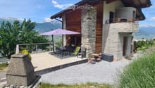 Two-story house with stone and wood exterior, balcony, outdoor dining area, and scenic mountain view.