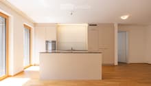 Modern kitchen with light-colored cabinets, a central island, and a built-in oven. The space features wooden flooring and large windows allowing natural light to fill the room.