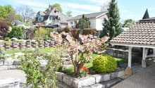 Well-maintained garden with a stone wall, flowering trees, shrubs, and a patio area with outdoor furniture.