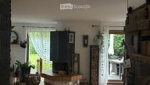 Bright living room with tiled floor, fireplace, large windows with curtains, and outdoor seating area visible through the glass doors.
