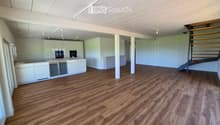 Open-plan space with light-colored wooden flooring, white cabinetry, and a staircase leading to an upper level. The area is unfurnished and appears to be a combined living and kitchen area.