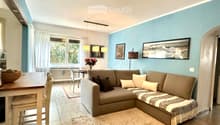 Modern living room with a grey sectional sofa, coffee table, dining table, chairs, and decorative items including a flower vase and picture frames.