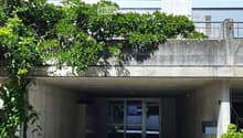 Modern concrete building with a covered entrance, greenery on the roof, and a spacious driveway.